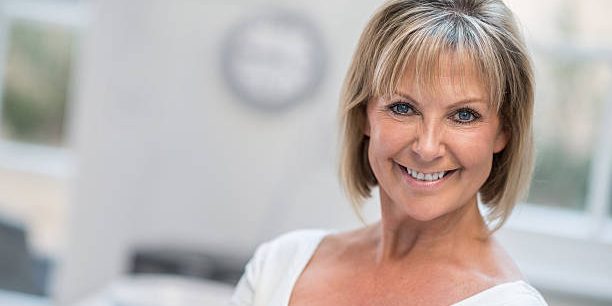 Smiling mature patient after All on 4 dental implants, bright clinic background, professional tone